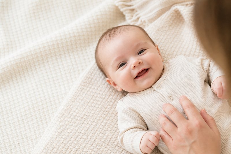 Awake two-to-three-month-old baby showing a natural social smile on a supervised soft blanket