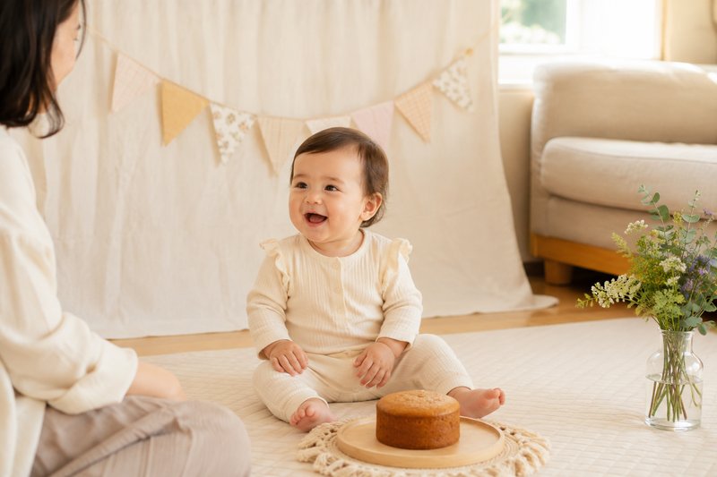 One-year-old seated safely on a floor mat beside a simple home birthday setup