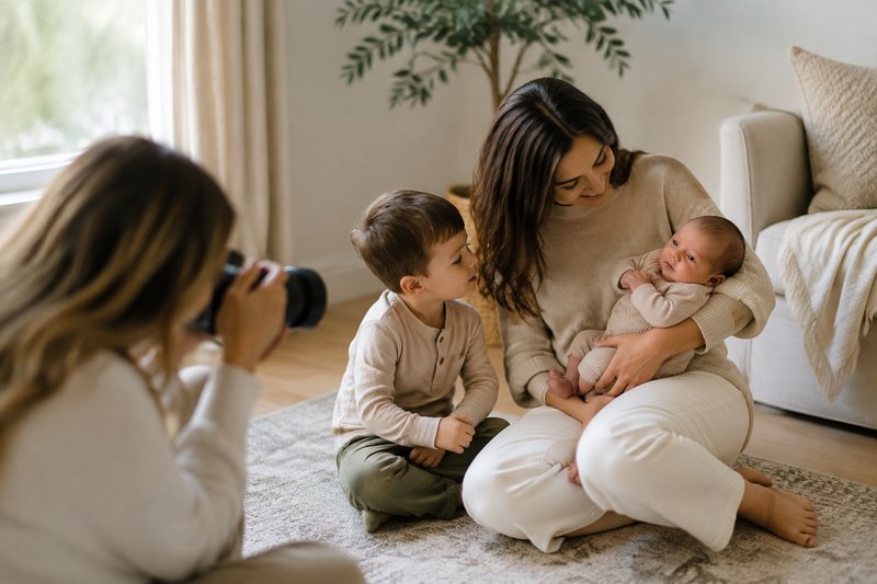 Older sibling beside a parent safely holding an awake newborn during an at-home photo session